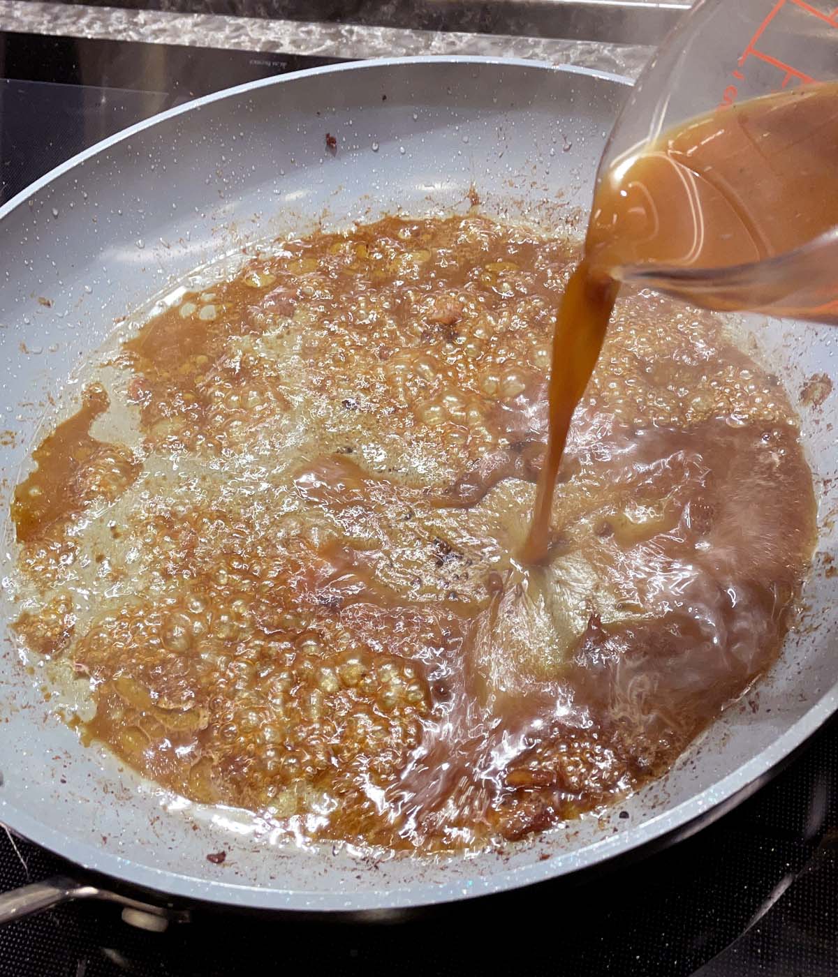 Brown liquid being poured and bubbling in a grey skillet.