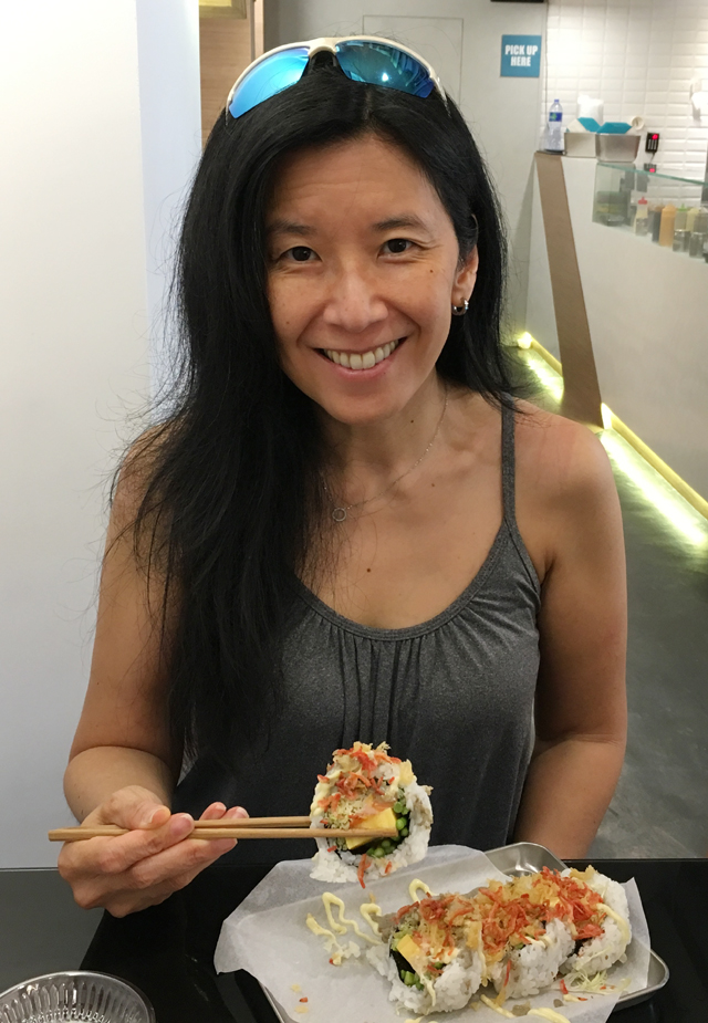 An Asian woman holding up a piece of maki sushi at Chotto Maki