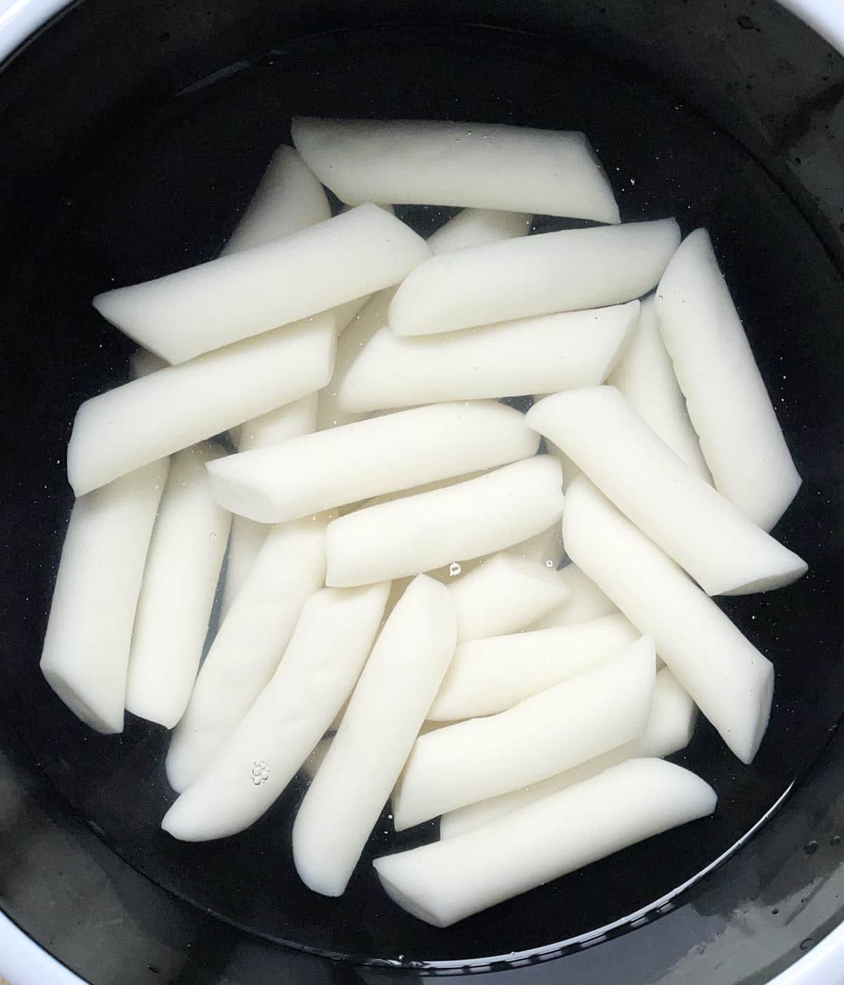 White cylinder shaped rice cakes in water in a black bowl.