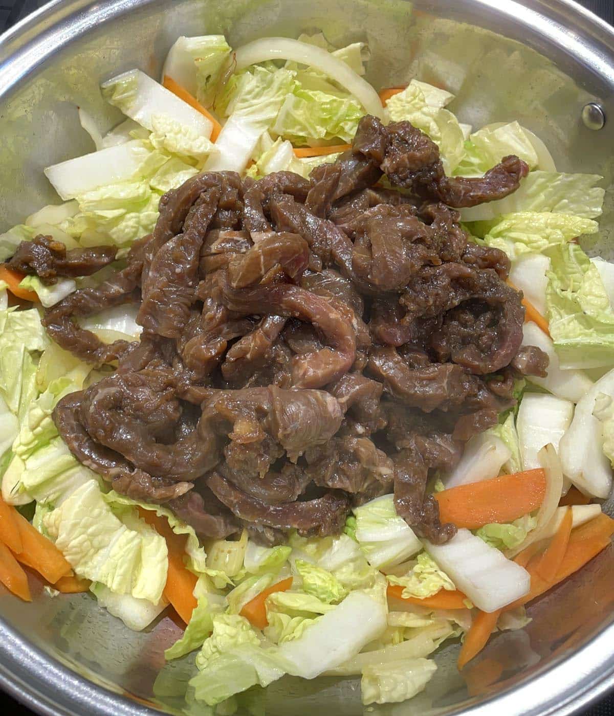 Brown beef slices and vegetables in a metal pan.
