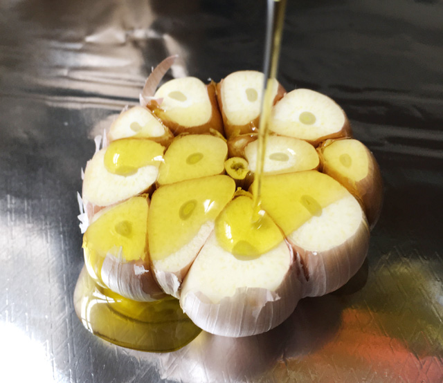 Olive oil being drizzled on a cut bulb of garlic for roasted garlic
