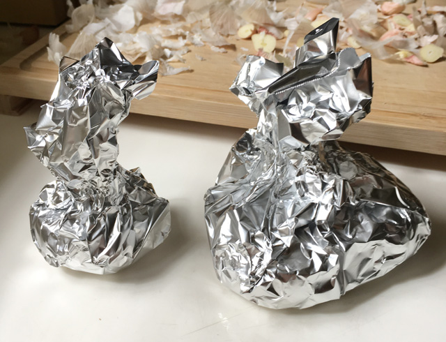 Two silver foil bundles containing garlic for roasted garlic