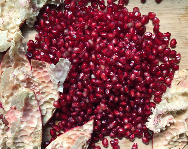 A large pile of pomegranate seeds surrounded by the empty skins on a wooden cutting board