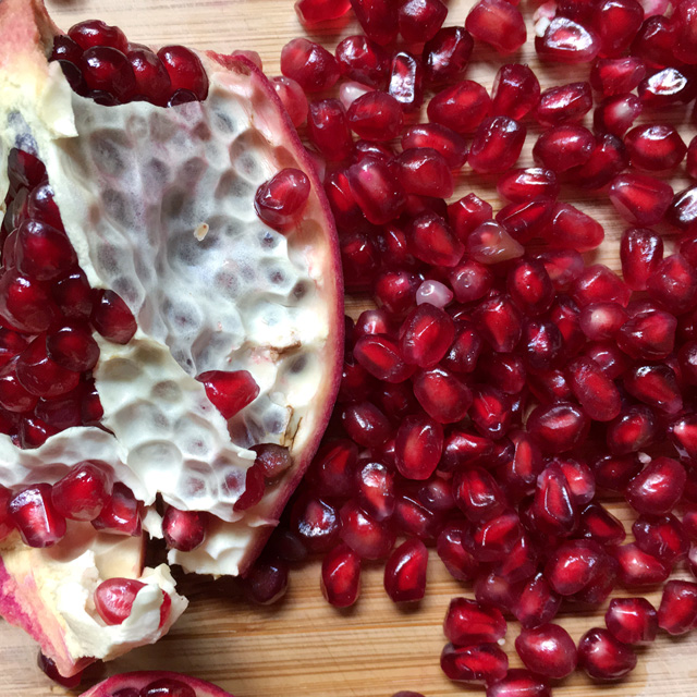 Close-up of a section of pomegranate next to a pile of pomegranate seeds