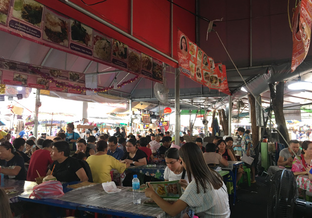 A crowd of people eating in a covered area at the Chatuchak Market, Bangkok