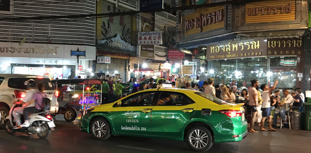 A yellow and green taxi driving by a large crowd of people