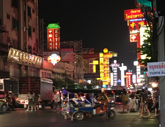 Many cars driving down a road lined with bright neon signs
