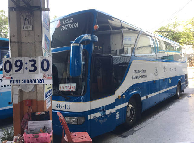 A blue and white bus parked next to a concrete post with a sign saying 9:30