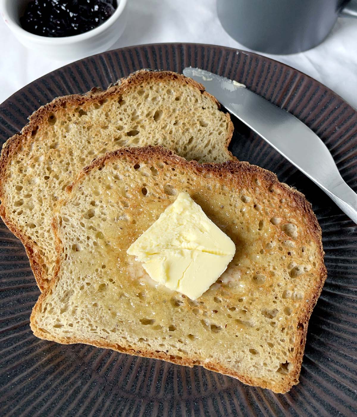 A pat of butter on two slices of toast on a dark brown plate.