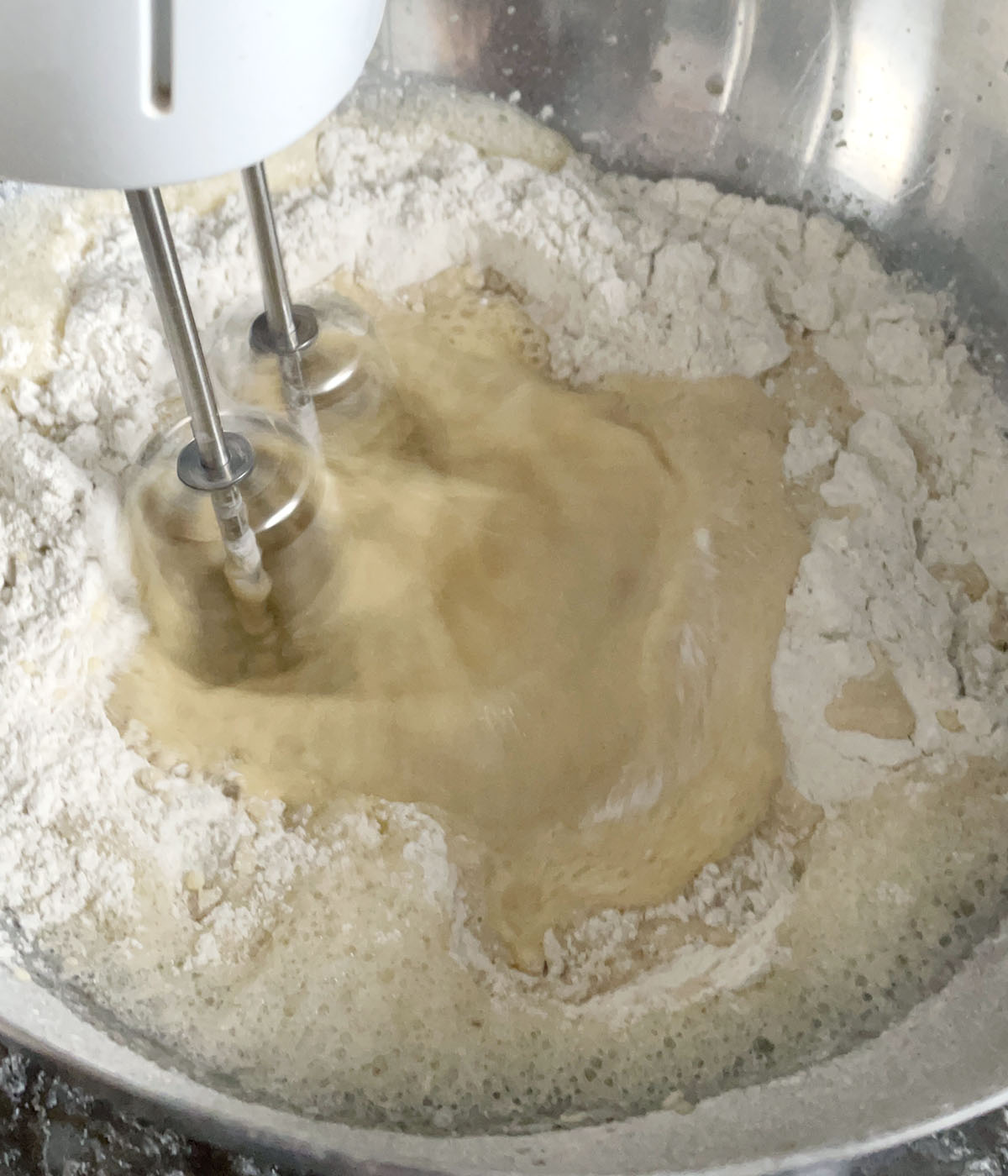 A mixer blending wet and dry ingredients in a round metal bowl.