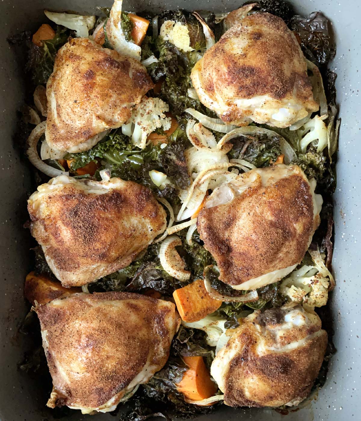 Six pieces of roasted chicken on a bed of vegetables in a rectangular roasting pan.