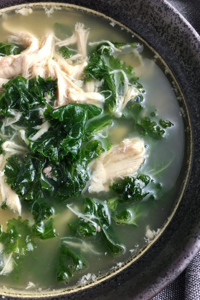 Close-up of a dark grey round bowl containing chicken kale soup