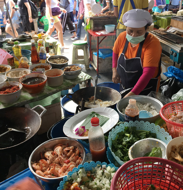 A woman wearing a face mask and cooking food in a round wok at the Chatuchak Market in Bangkok