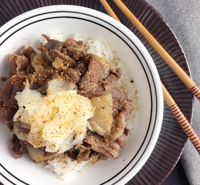 A white round bowl containing beef and onions on top of white rice for gyudon beef bowl