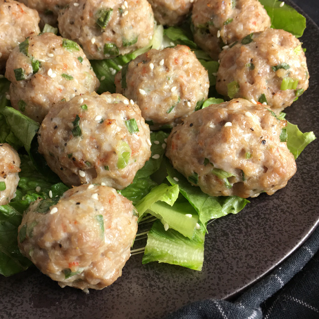 A dark round plate containing pork and shrimp meatballs on chopped green lettuce