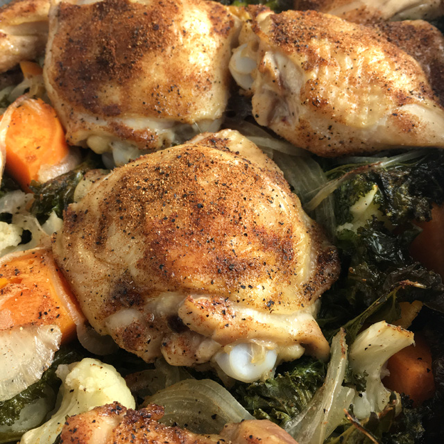 Close-up of chicken pieces resting on a bed of roast kale, onions, sweet potatoes, and cauliflower