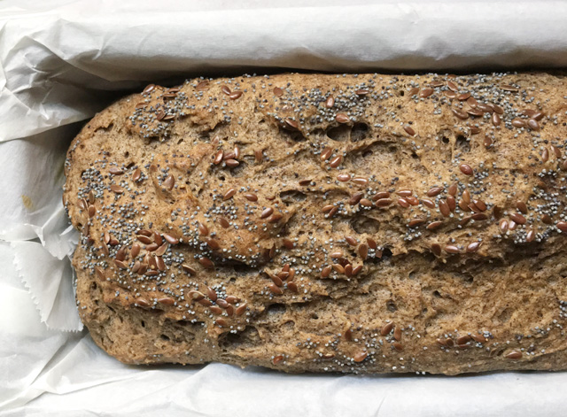 A brown loaf of buckwheat bread in a baking pan lined with white parchment paper