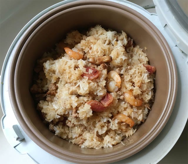 A brown metal pot containing rice, shrimp, mushrooms, and sausages for Chinese sticky rice