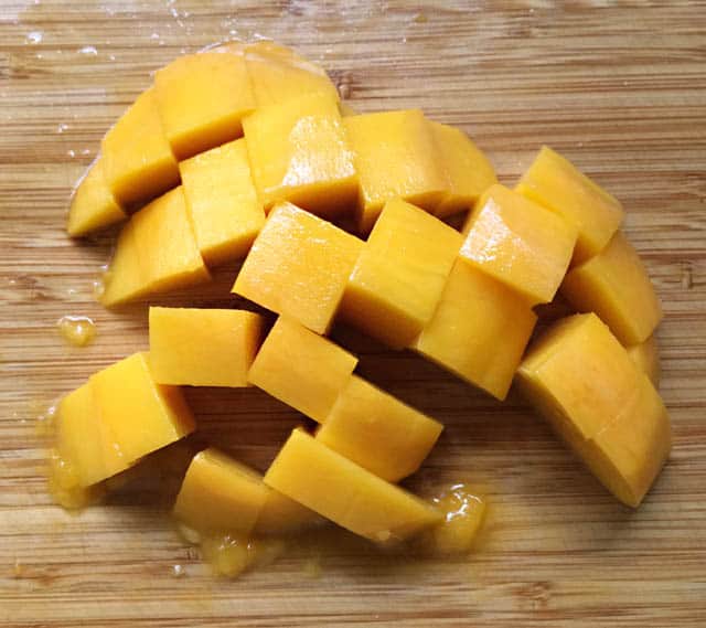 Cubed chunks of yellow orange mango on a wooden cutting board