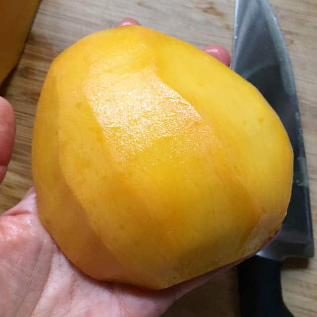 A hand holding a large section of peeled yellow orange mango