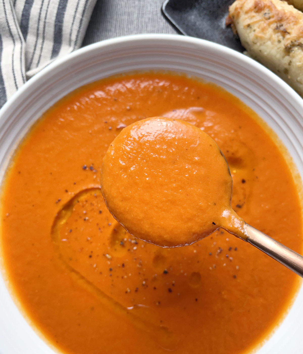Close-up of a spoonful of orange roasted tomato soup over a white bowl.