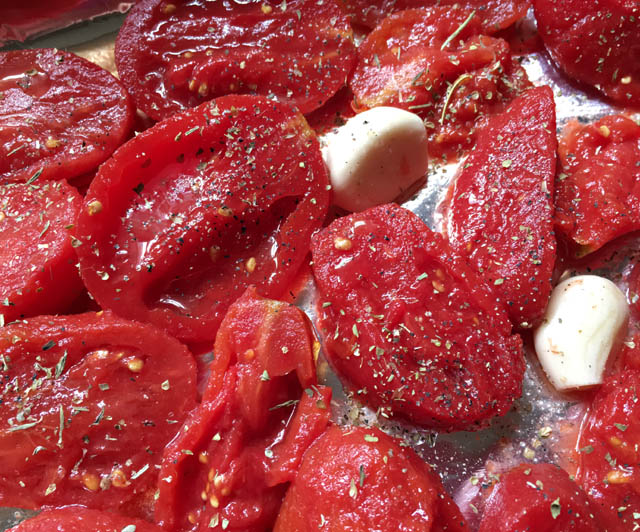 Several red tomato halves and white garlic cloves on a metal baking sheet for roasted tomato soup