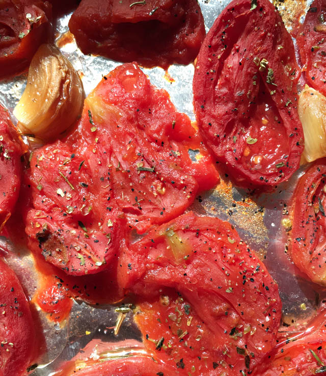 Red tomatoes and brown garlic cloves on a baking sheet for roasted tomato soup