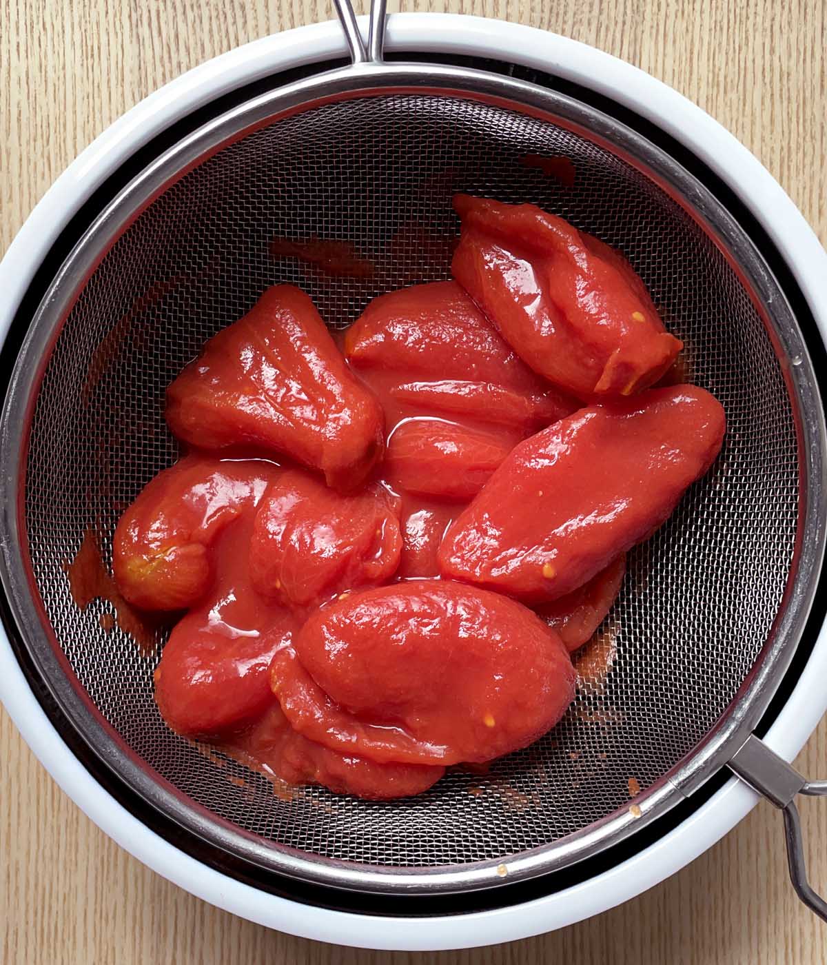 Red tomatoes in a strainer over a bowl.