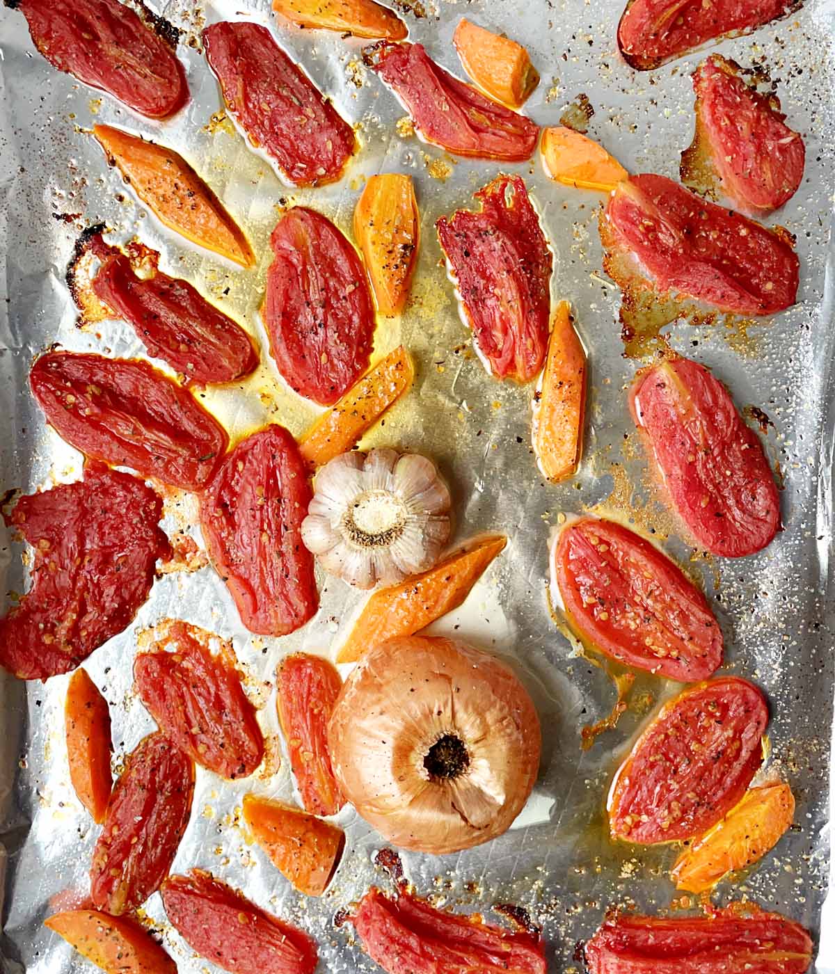 Roasted tomatoes, carrots, garlic, and onion on a foil-lined baking sheet.