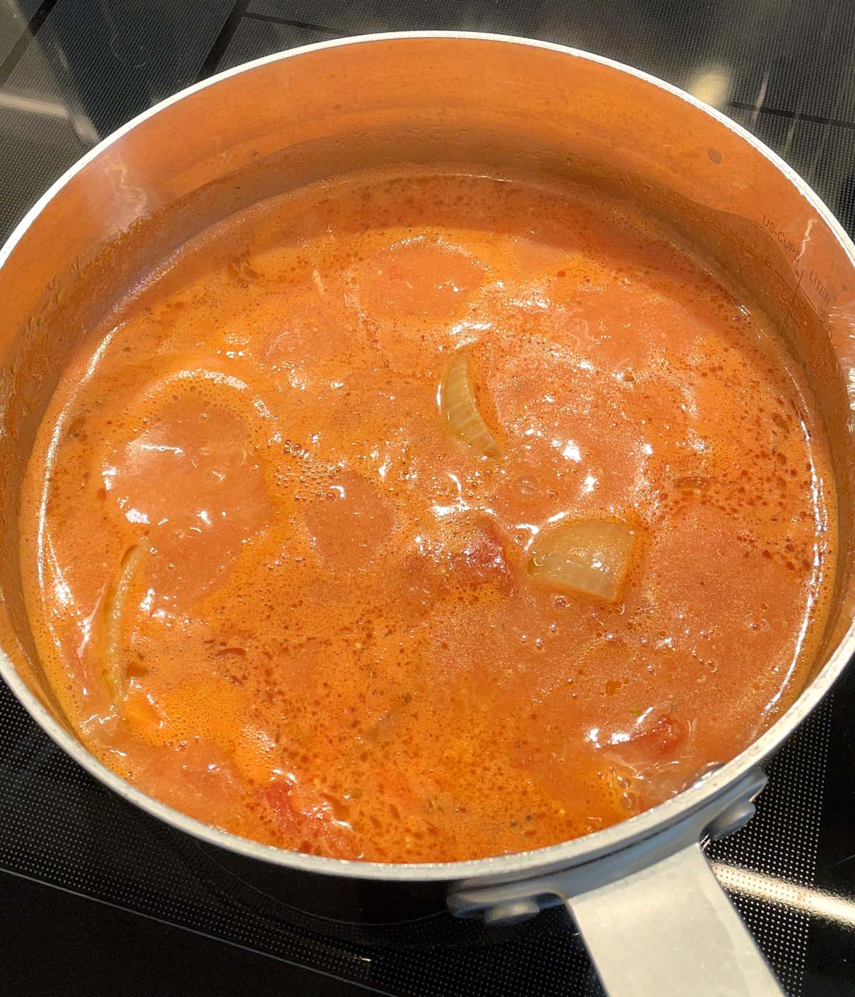 A metal pot containing boiling orange roasted tomato soup.