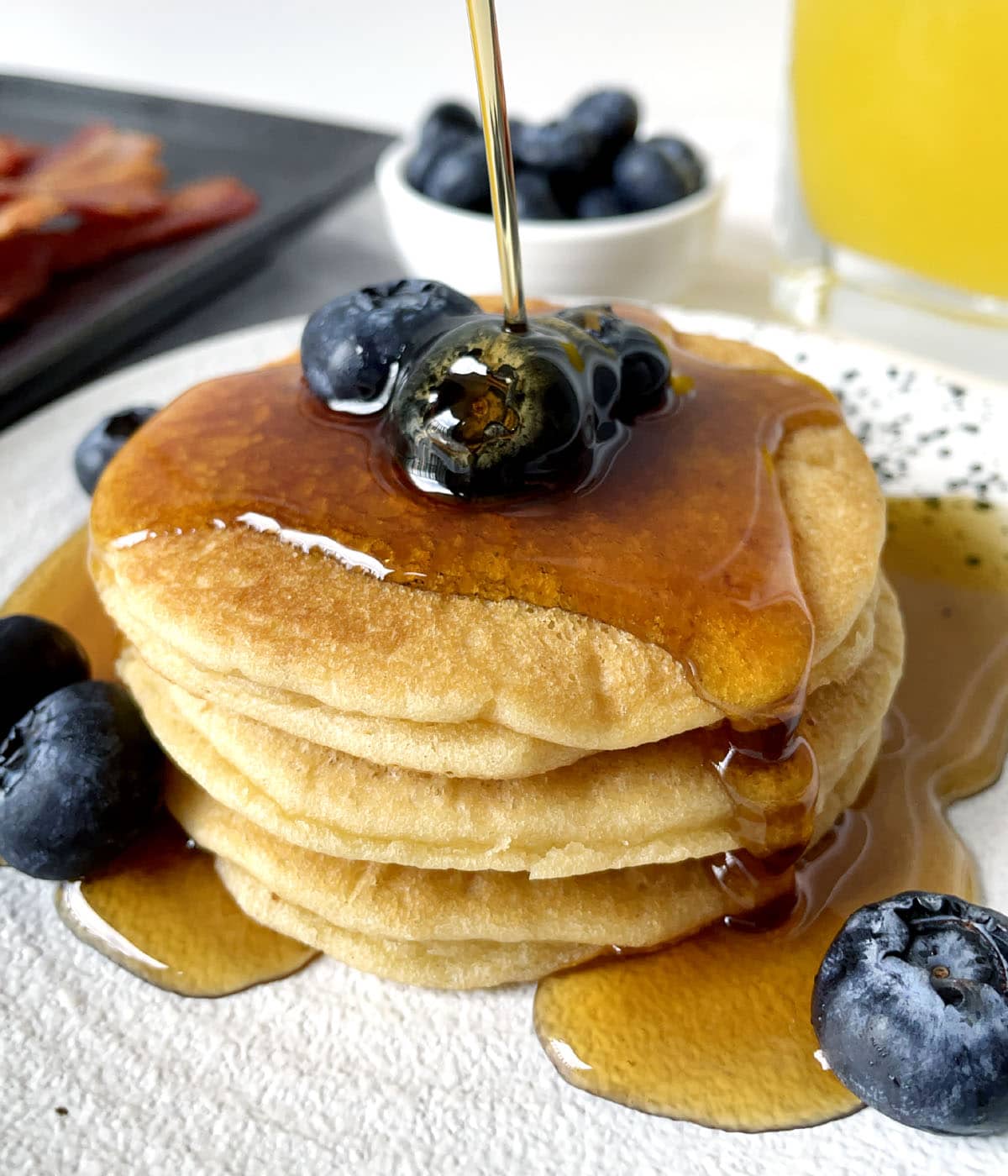 Brown syrup being poured over a stack of three pancakes topped with blueberries.