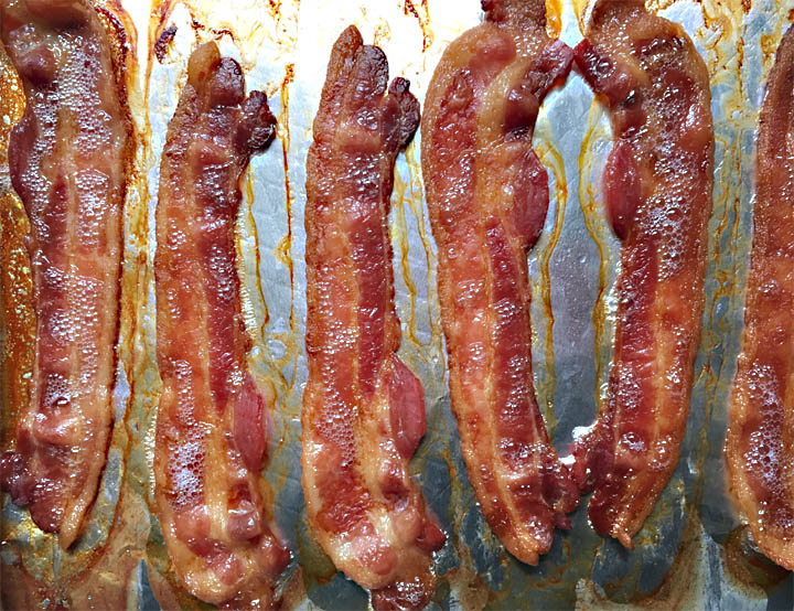 Six slices of cooked bacon on a foil-lined baking pan