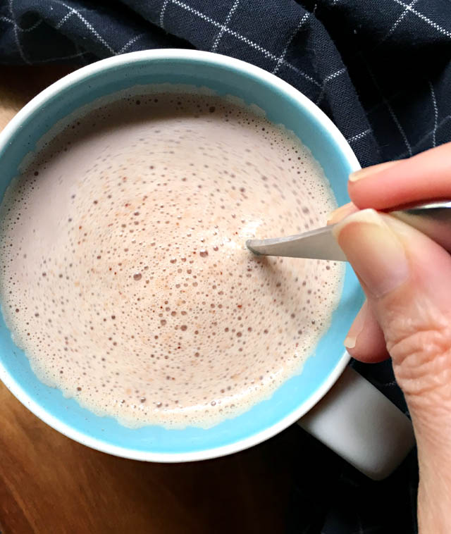 A hand stirring a spoon in a blue and white mug containing chocolate peppermint tea latte