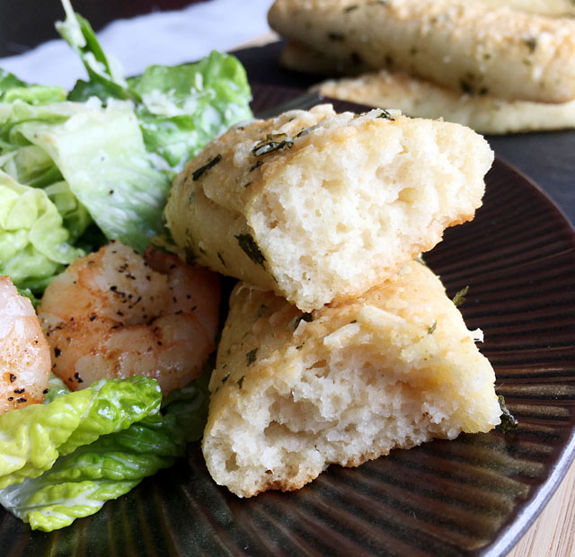 A breadstick ripped in half next to a green salad and pink shrimp on a brown plate