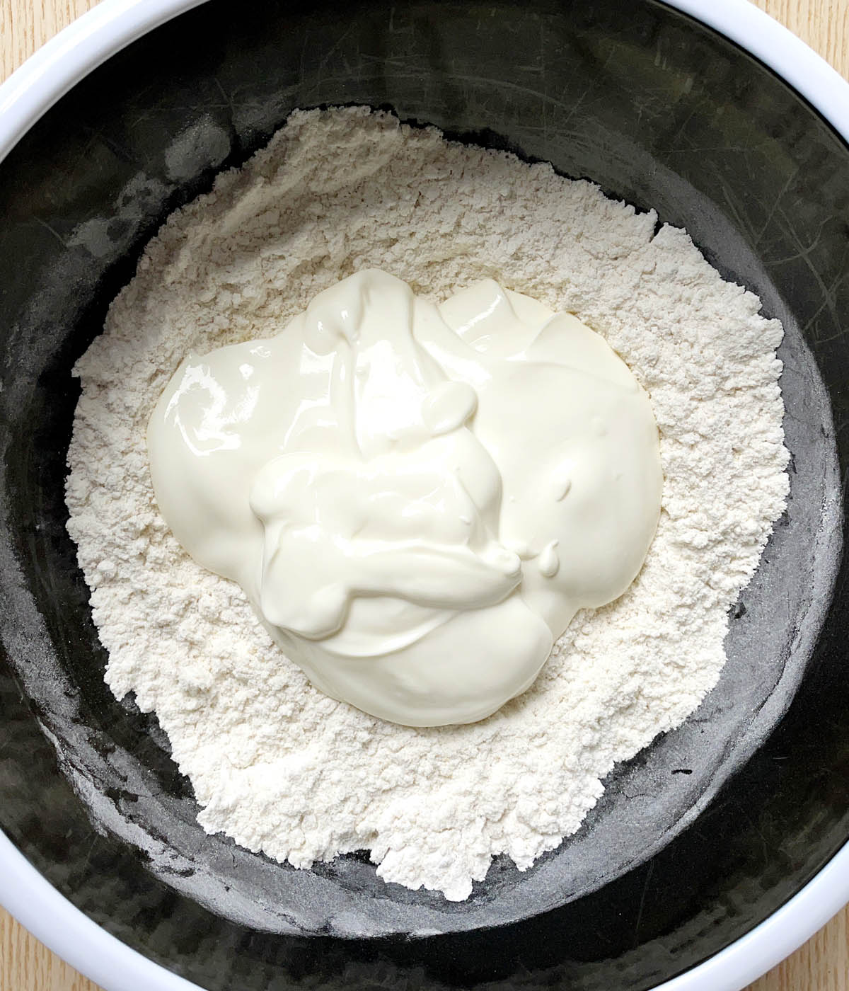 A round black bowl containing white flour and white yogurt.