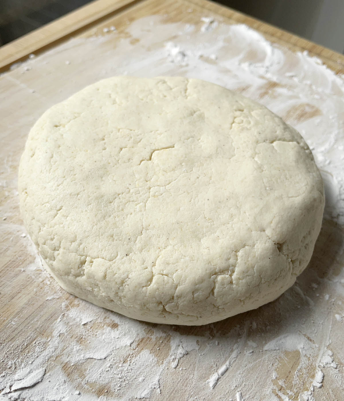 A disc shaped piece of dough on a floured wooden cutting board.