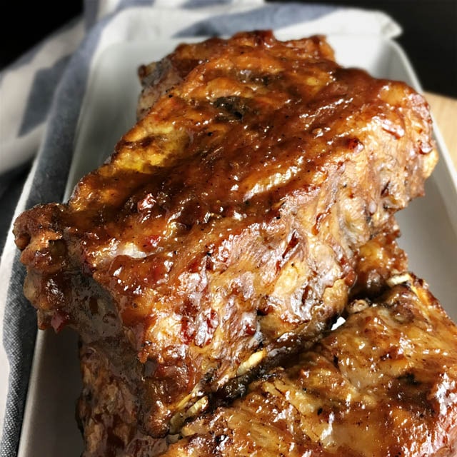 A white rectangular plate containing brown glazed ribs
