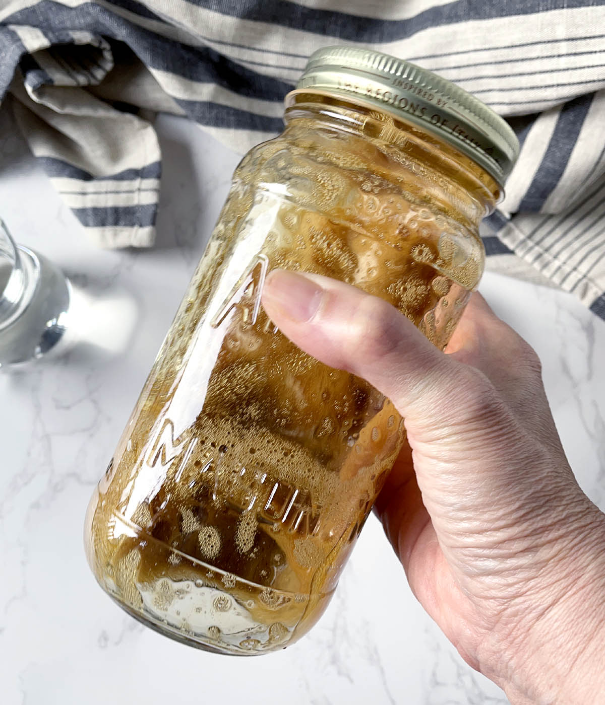 A hand holding a jar containing bubbly brown liquid.
