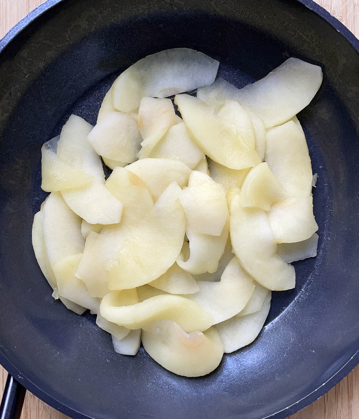 Cooked, wilted apple slices in a dark skillet.