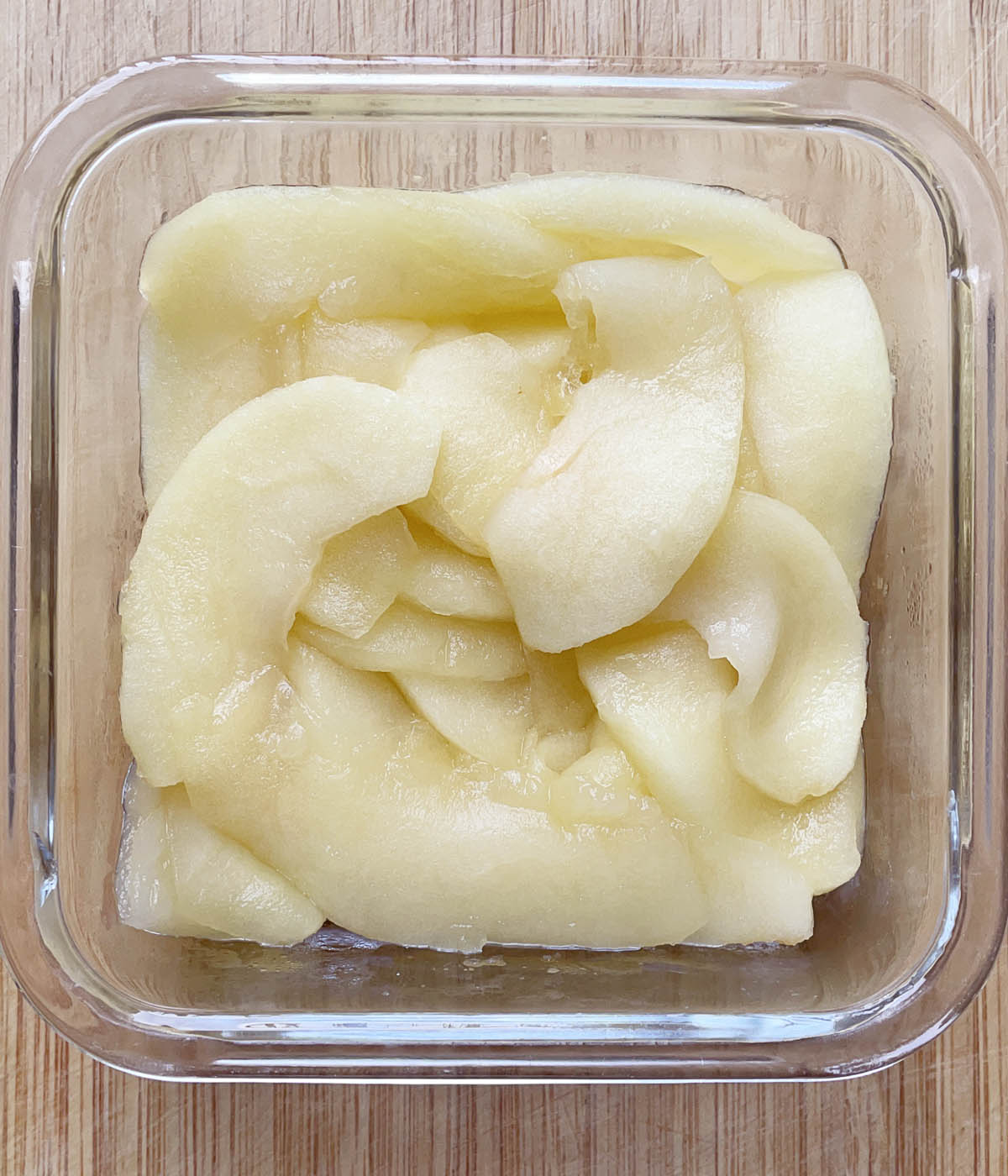 Cooked apple slices packed in a square glass container.