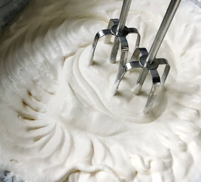 Two metal mixer beaters leaving trails in thickened whipped cream in a bowl