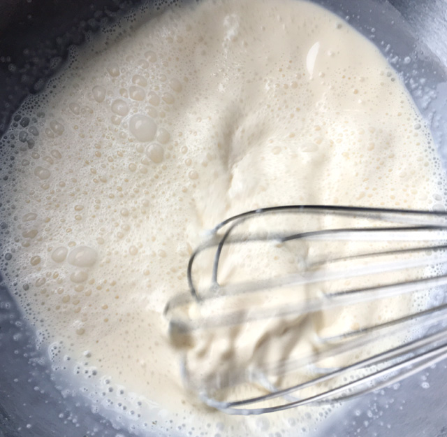 A metal whisk whipping white cream in a metal bowl