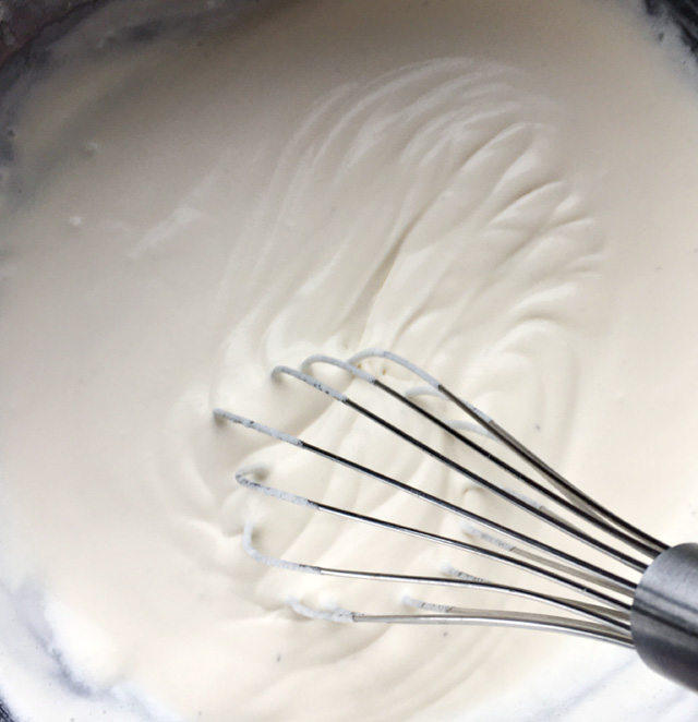 A metal whisk in a bowl containing thickened white cream