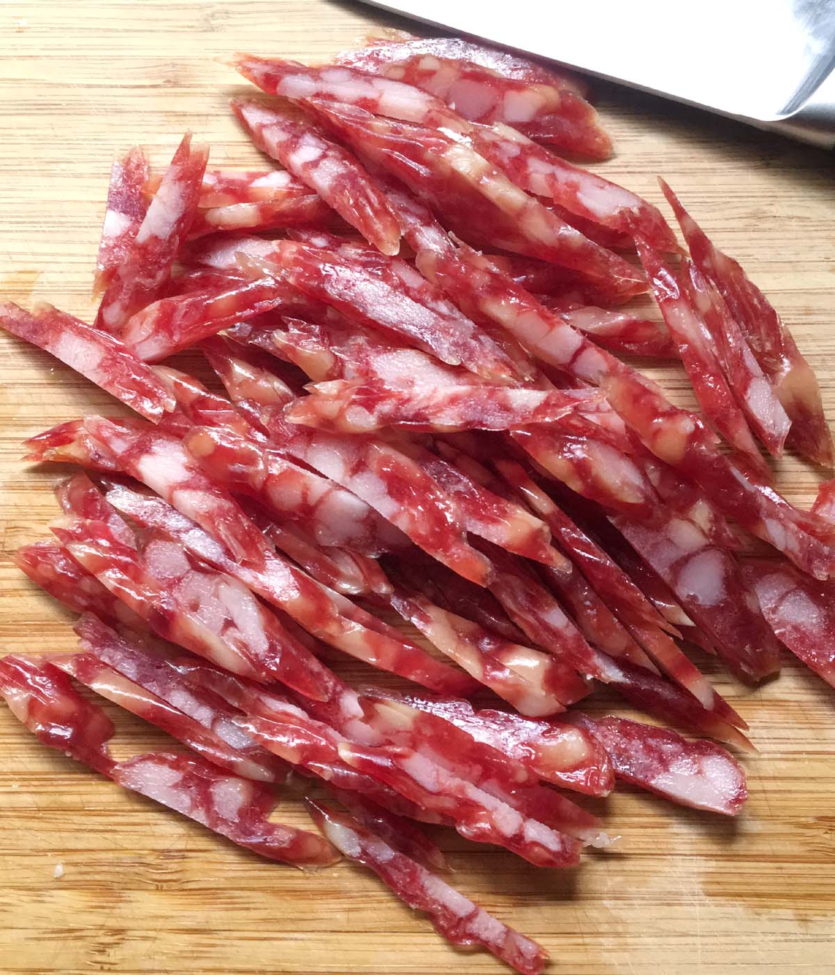 Red sausage cut into strips on a wooden cutting board.