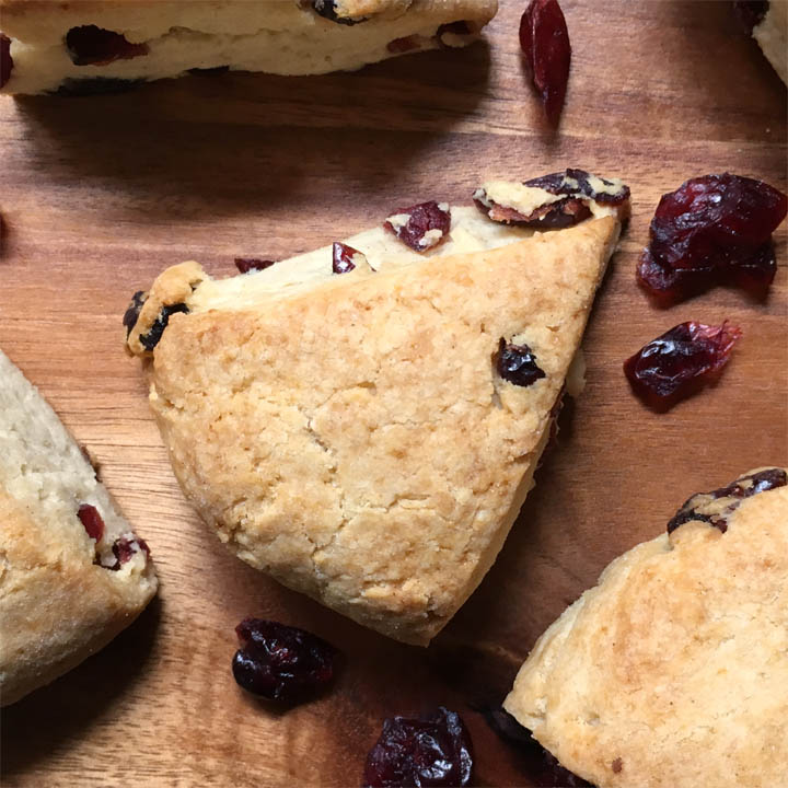 Close-up of a cranberry scone wedge and dried cranberries on a wood board