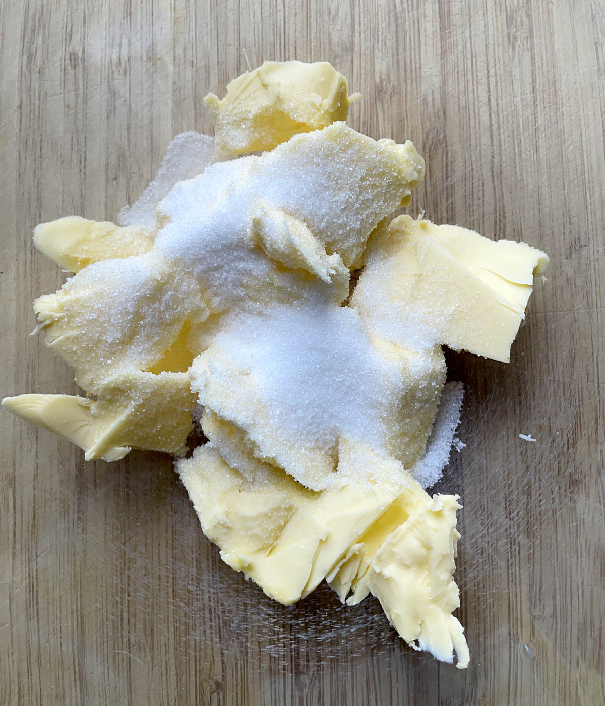 White sugar and yellow butter chunks in a glass bowl on a wooden cutting board.