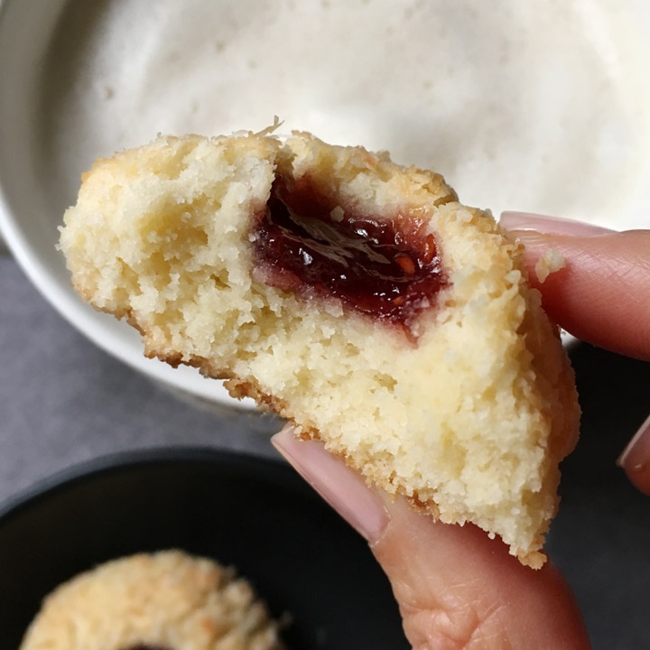 Closeup of a hand holding a jam cookie with a bite taken out