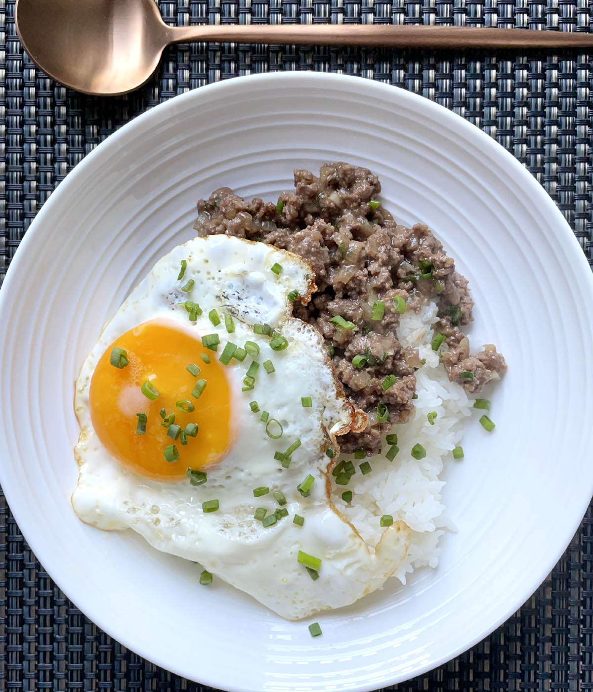 A round white dish containing white rice, ground meat, a sunny-side up fried egg, and chopped green onions.