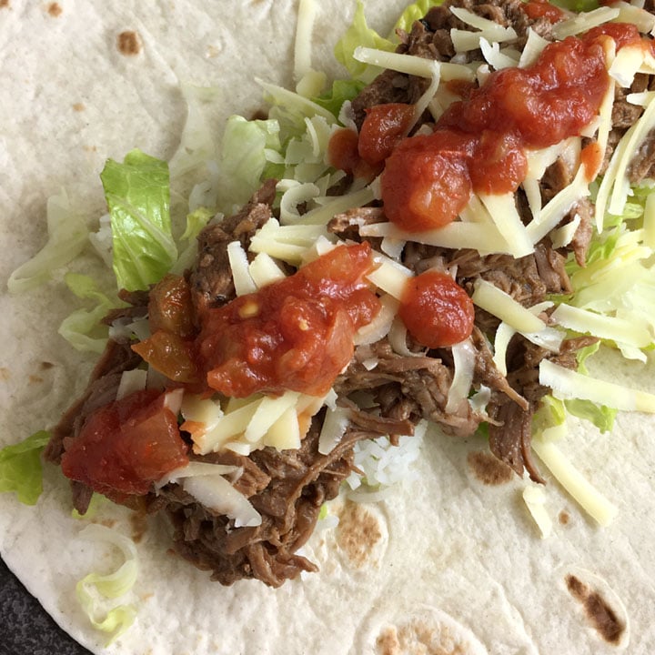 Brown shredded beef, grated white cheese, green lettuce, red salsa, on a flour tortilla