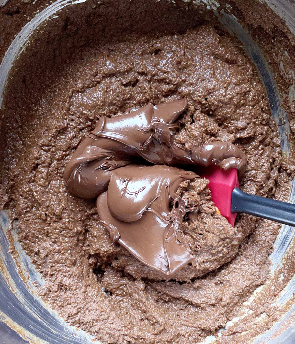 A metal bowl containing a rubber spatula and brown cake batter and melted chocolate.